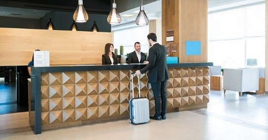 مسافری چمدان به دست پشت پیشخوان پذیرش هتل