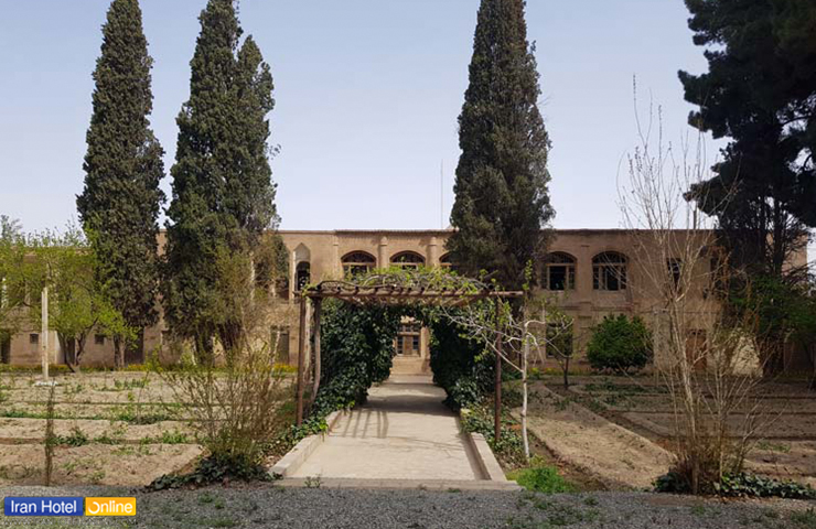 نمایی زیبا از باغ و عمارت رحیم آباد بیرجند در فصل بهار با درختان سرو و ساختمان آجری